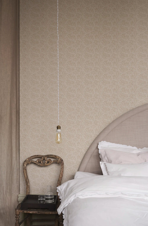Coral wallpaper by Sandberg in tonal sand, small coral-branch motif styled behind a linen bed with antique chair and pendant