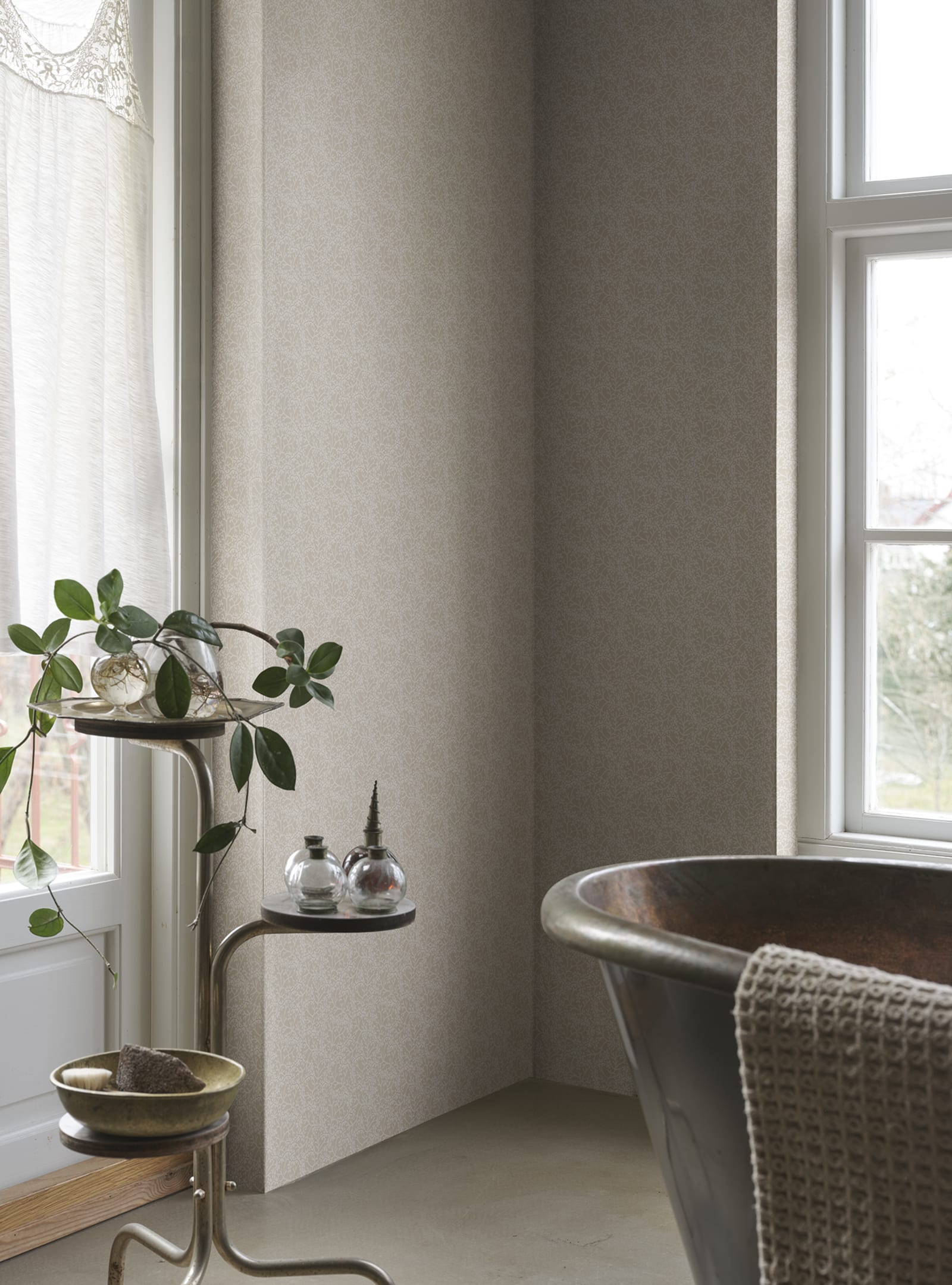 Coral wallpaper by Sandberg in sand tones, styled in a bathroom corner beside a copper tub and plant stand by the window