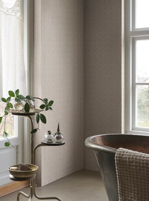 Coral wallpaper by Sandberg in sand tones, styled in a bathroom corner beside a copper tub and plant stand by the window