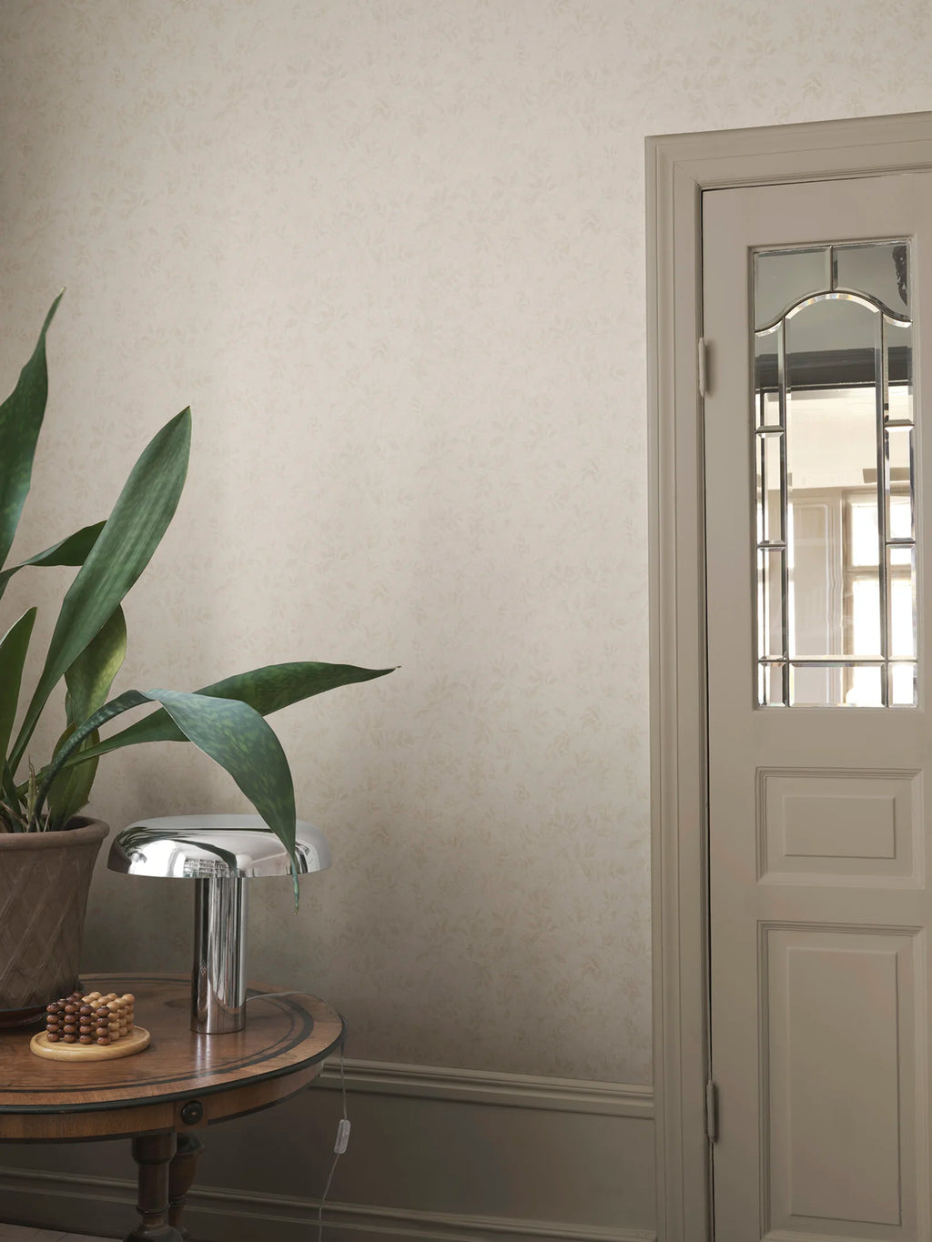 Mila wallpaper by Sandberg in tonal cream, styled in a hallway corner behind a snake plant and chrome mushroom lamp