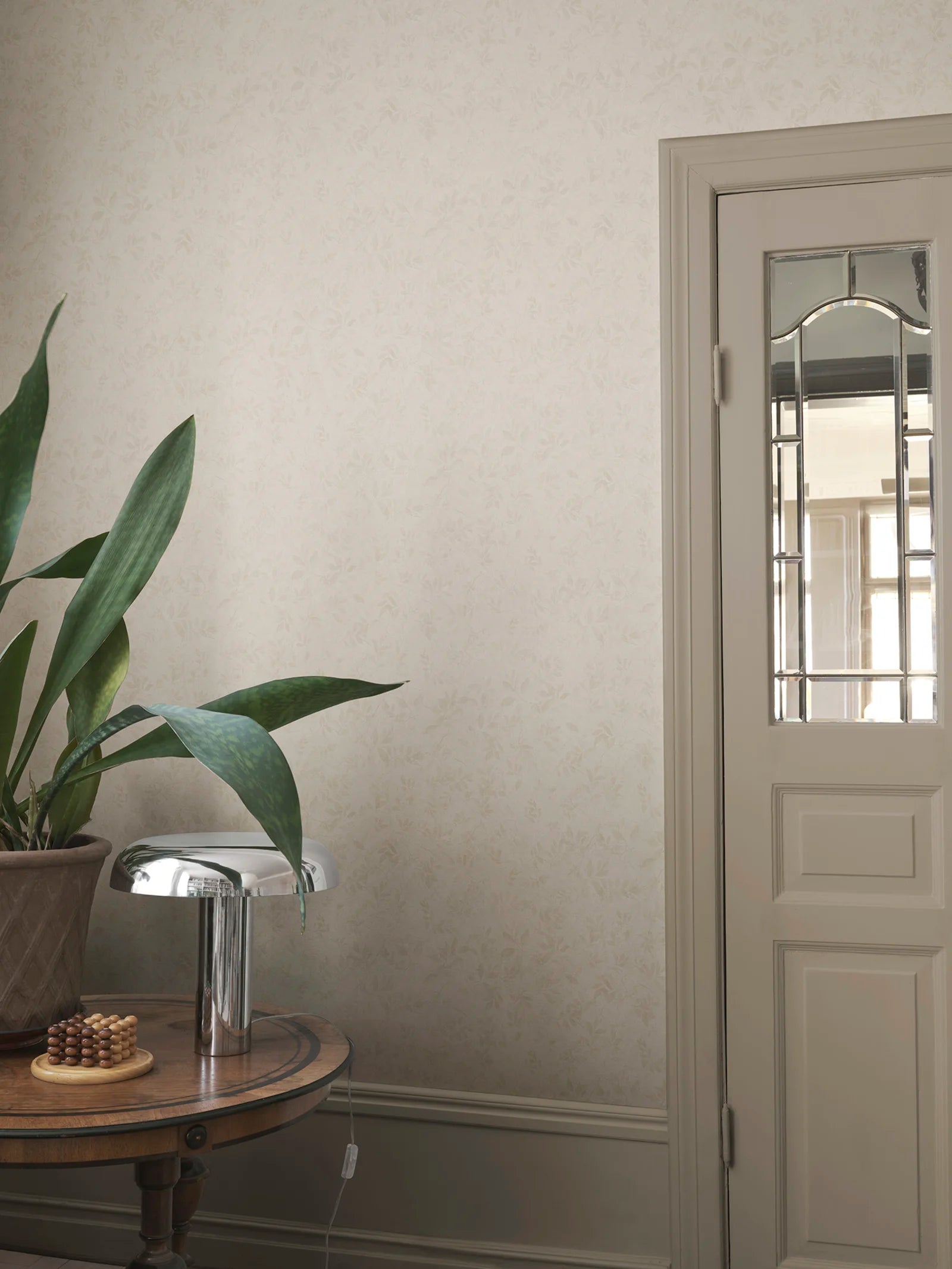 Mila wallpaper by Sandberg in tonal cream, styled in a hallway corner behind a snake plant and chrome mushroom lamp