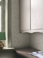 Mila wallpaper by Sandberg in sage on cream, styled in a study nook by a window with a green lamp and scalloped cabinet