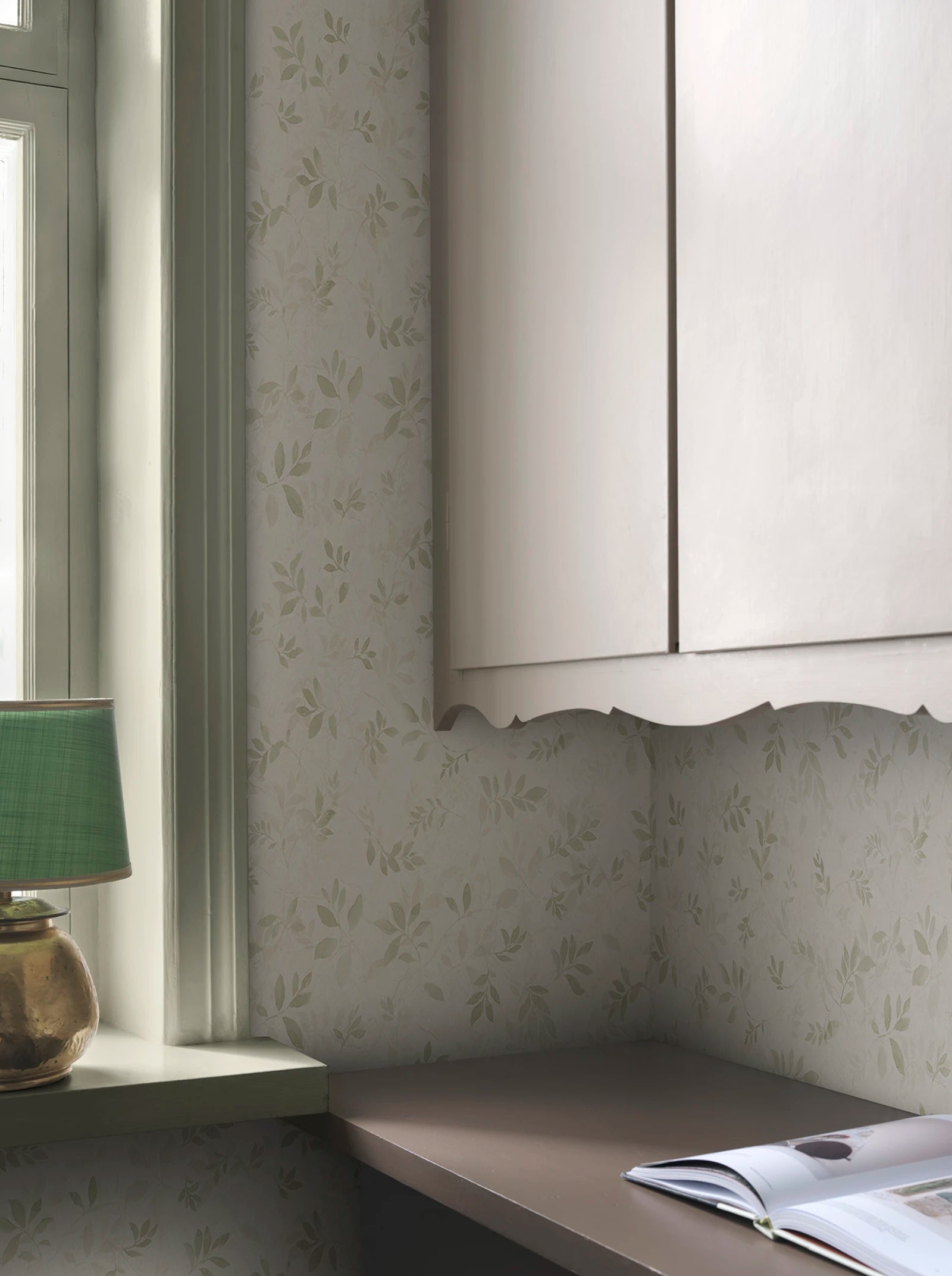 Mila wallpaper by Sandberg in sage on cream, styled in a study nook by a window with a green lamp and scalloped cabinet