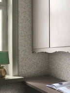 Olivia wallpaper by Sandberg in sage-green olive branches on cream, styled behind a window and kitchen cabinetry with a green lamp