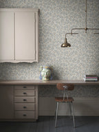 Olivia wallpaper by Sandberg in blue-grey olive branches, styled in a home office with desk, brass lamp and ceramic head vase
