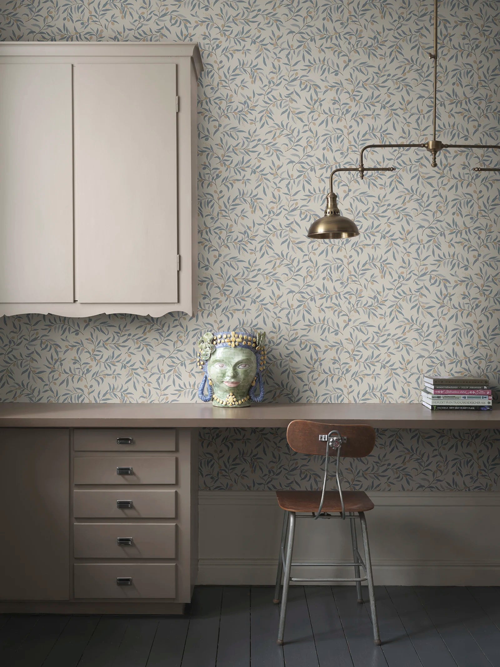 Olivia wallpaper by Sandberg in blue-grey olive branches, styled in a home office with desk, brass lamp and ceramic head vase