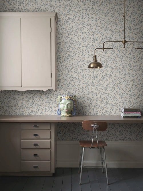 Olivia wallpaper by Sandberg in blue-grey olive branches, styled in a home office with desk, brass lamp and ceramic head vase