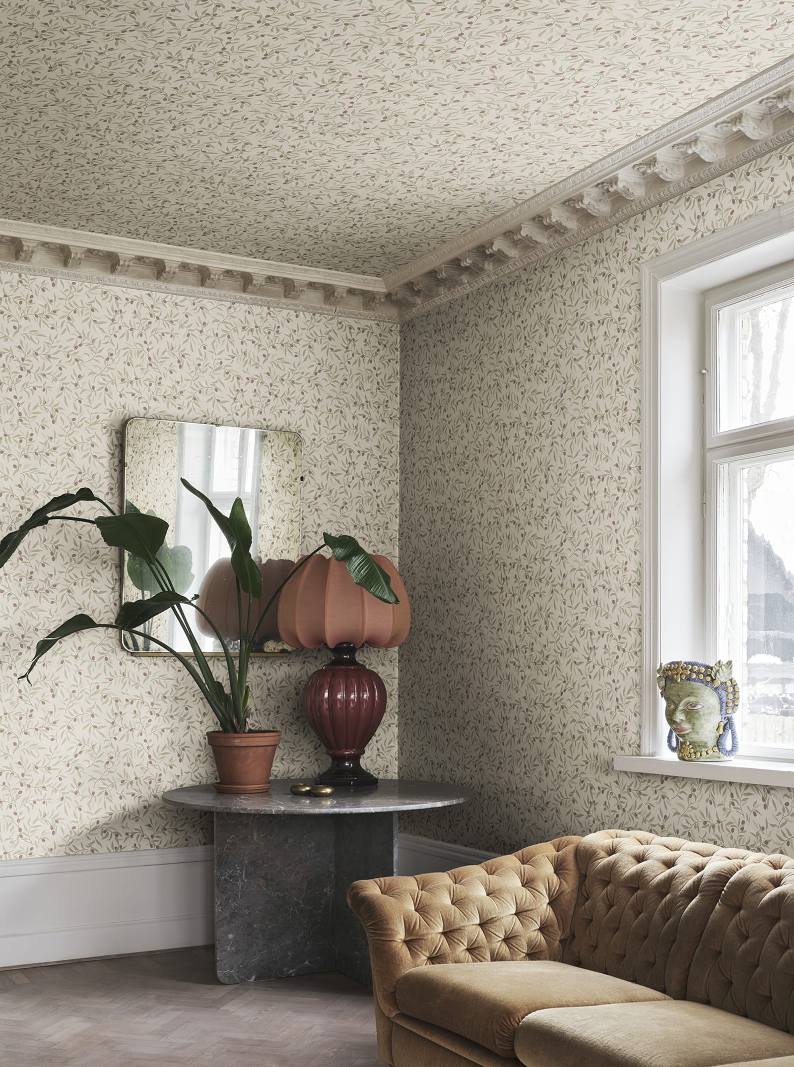 Olivia wallpaper by Sandberg in muted green olive sprigs covering walls and ceiling of a corner sitting room with velvet sofa