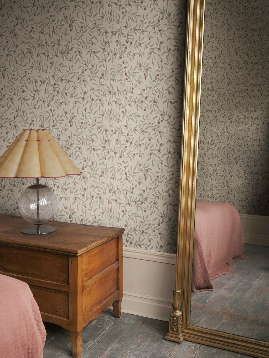 Olivia wallpaper by Sandberg in green-and-burgundy olive sprigs, styled in a bedroom with timber chest, lamp and gilt mirror