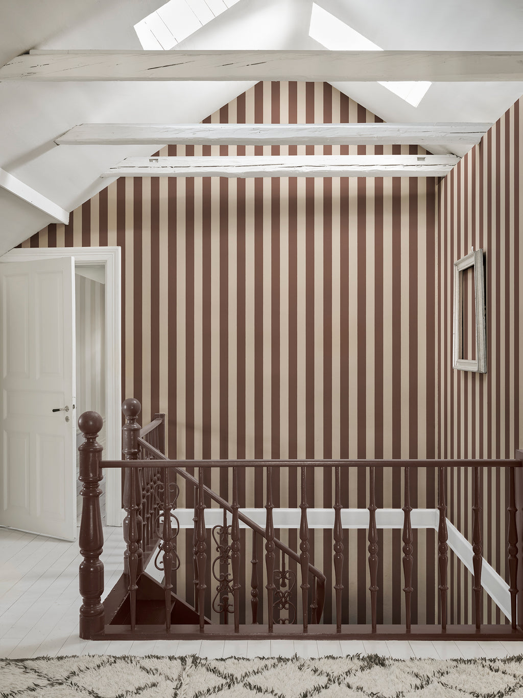 Brown striped Sam wallpaper by Sandberg on a vaulted landing above a dark wooden staircase