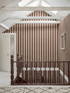 Brown striped Sam wallpaper by Sandberg on a vaulted landing above a dark wooden staircase