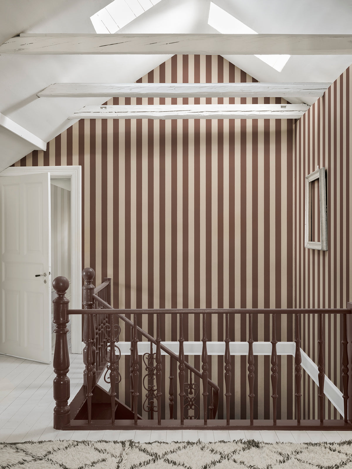 Brown striped Sam wallpaper by Sandberg on a vaulted landing above a dark wooden staircase