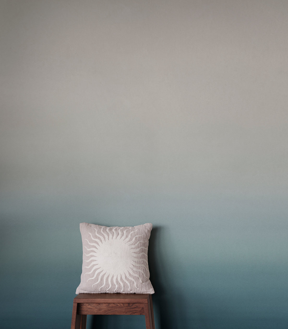 Skymning wall mural by Sandberg, cream-to-teal ombré sky styled behind a sunburst cushion on a timber stool