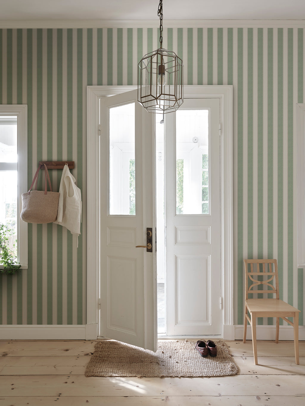 Henrik wallpaper by Sandberg in a hallway with white glazed doors and woven bag on a peg, green ticking-stripe pattern