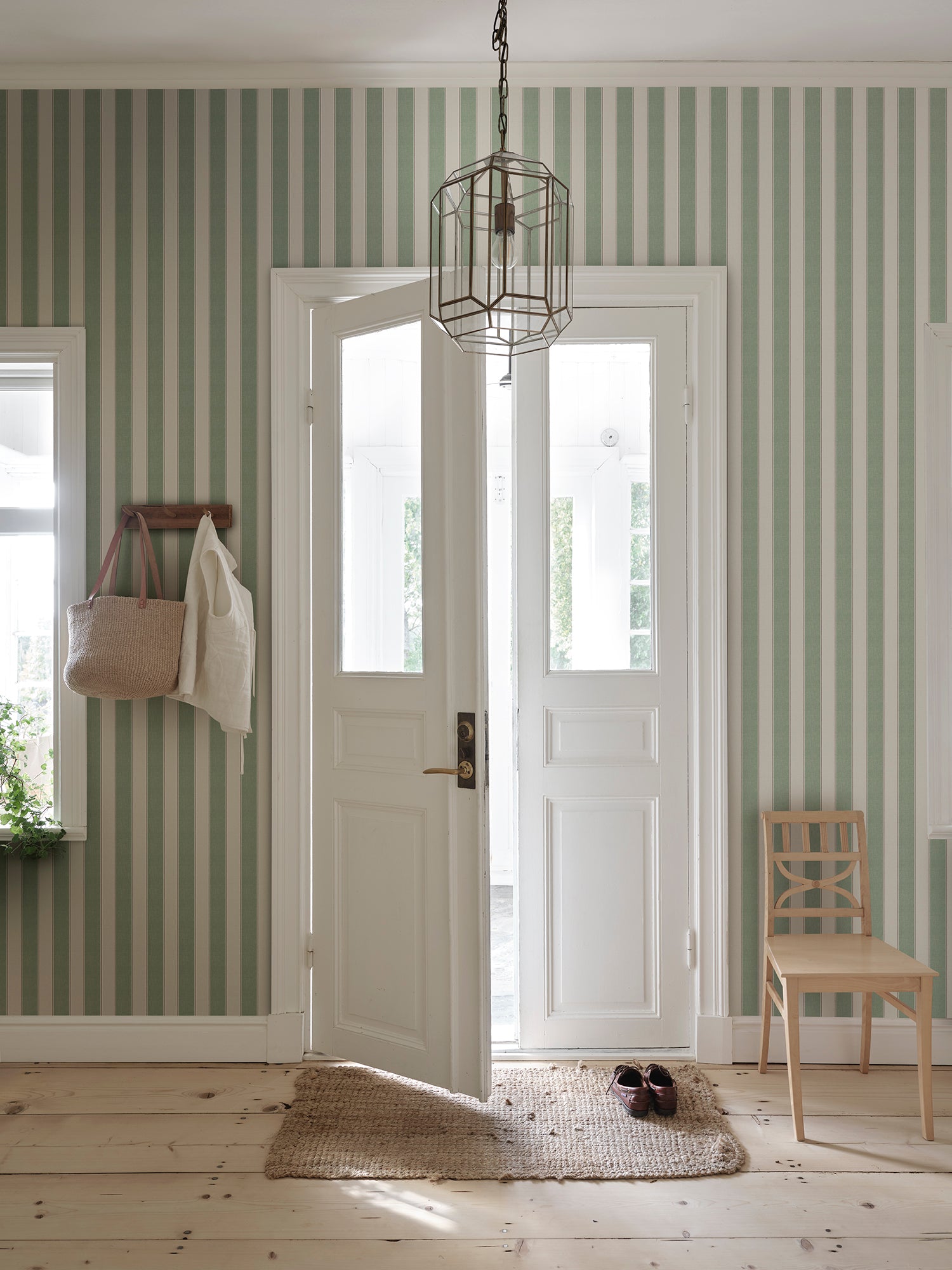 Henrik wallpaper by Sandberg in a hallway with white glazed doors and woven bag on a peg, green ticking-stripe pattern