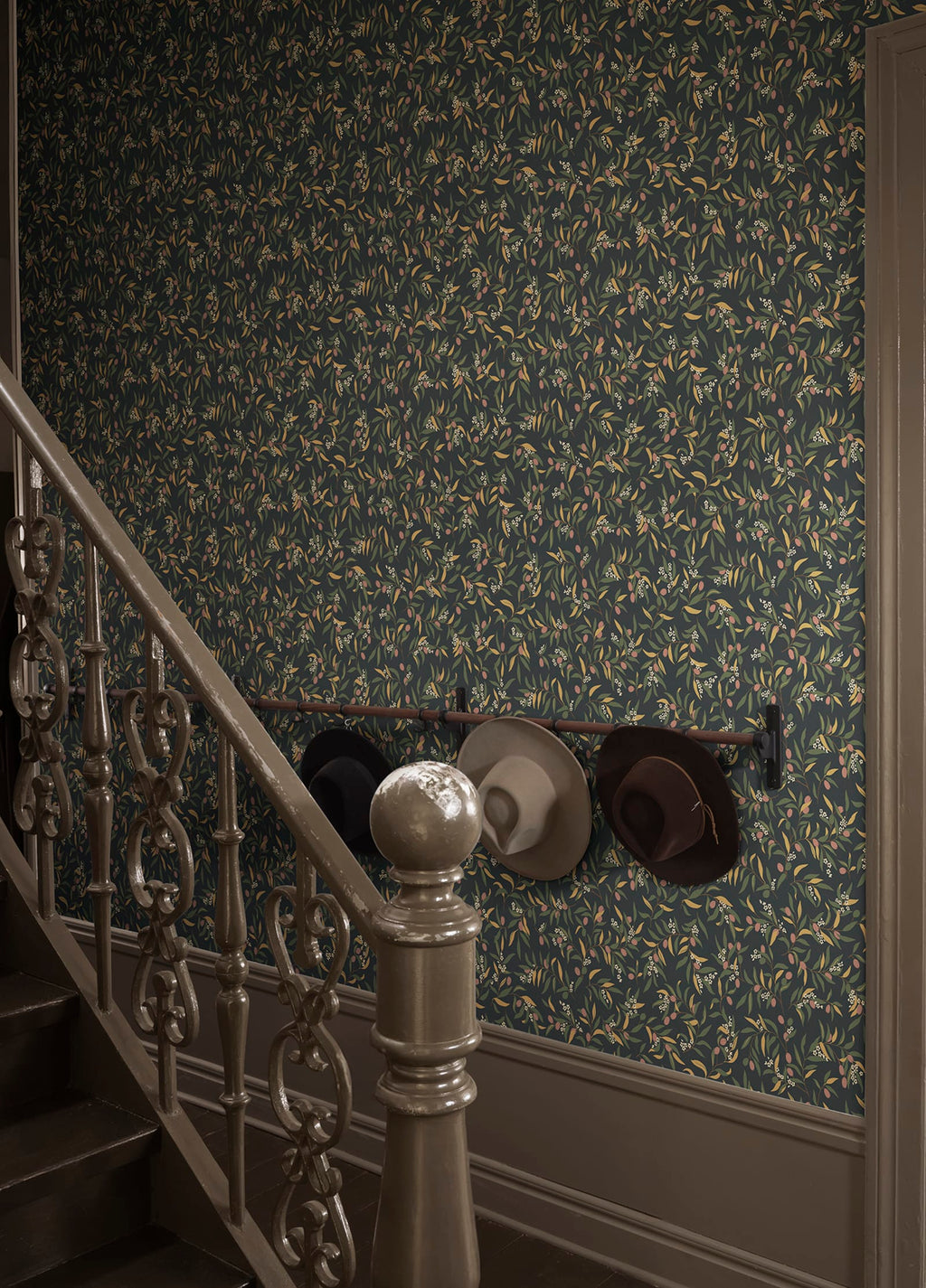 Olivia wallpaper by Sandberg in dark olive sprigs, styled on a stairwell wall with hats hung on a rail above panelling
