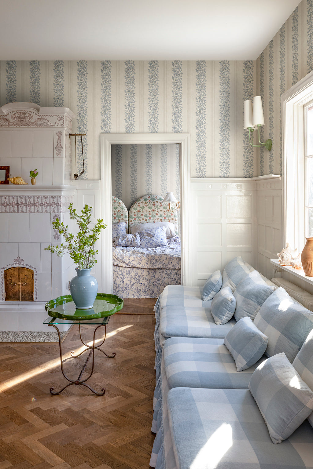 Natalie wallpaper by Sandberg styled in a sunlit living room with check sofa and green side table, blue floral-stripe design