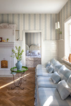 Natalie wallpaper by Sandberg styled in a sunlit living room with check sofa and green side table, blue floral-stripe design