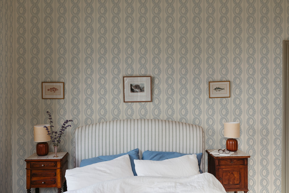 Emilion wallpaper by Sandberg in Blue behind a striped headboard in a calm bedroom with framed prints