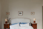 Elise wallpaper by Sandberg in Blue behind a striped headboard in a calm bedroom with framed prints