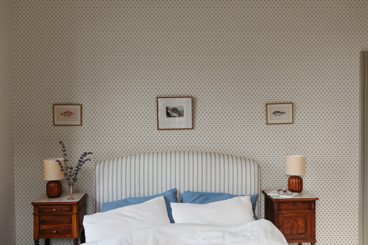 Elise wallpaper by Sandberg in Blue behind a striped headboard in a calm bedroom with framed prints