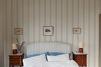 Austine wallpaper by Sandberg in Blue behind a striped headboard in a calm bedroom with framed prints
