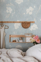 Poppy wallpaper by Sandberg in soft blue with white poppies, styled in a bedroom behind a wooden peg rail and shelf