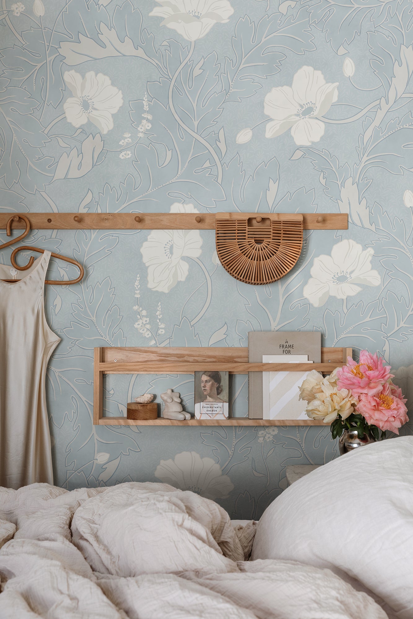 Poppy wallpaper by Sandberg in soft blue with white poppies, styled in a bedroom behind a wooden peg rail and shelf