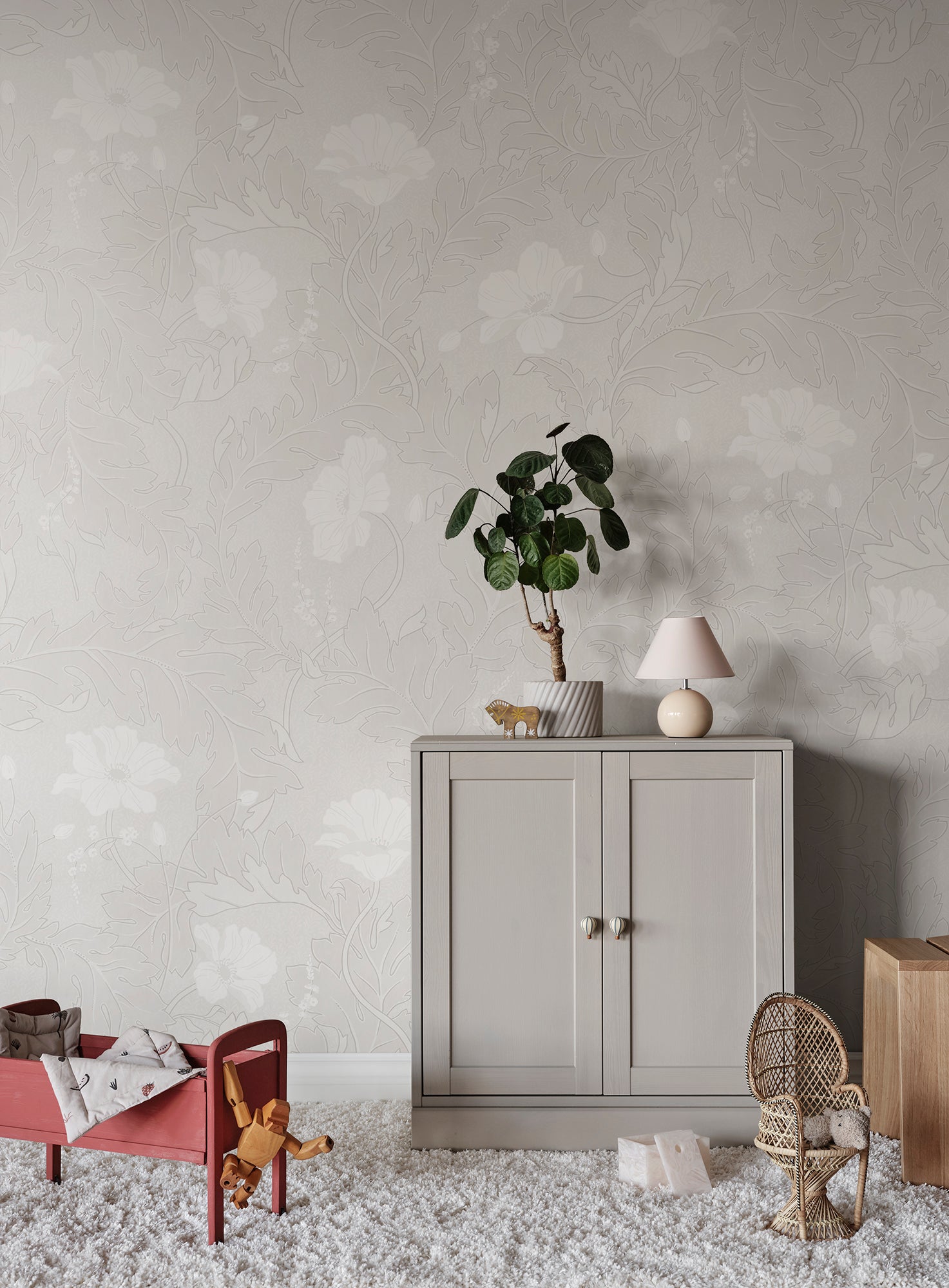 Poppy wallpaper by Sandberg in pale oatmeal, styled in a nursery behind a grey cabinet, red toddler bed and rattan chair
