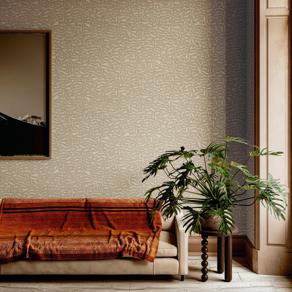 Kona wallpaper by Arte in Beige – Champagne behind a sofa with a rust throw and a large plant