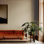 Kona wallpaper by Arte in Beige – Champagne behind a sofa with a rust throw and a large plant