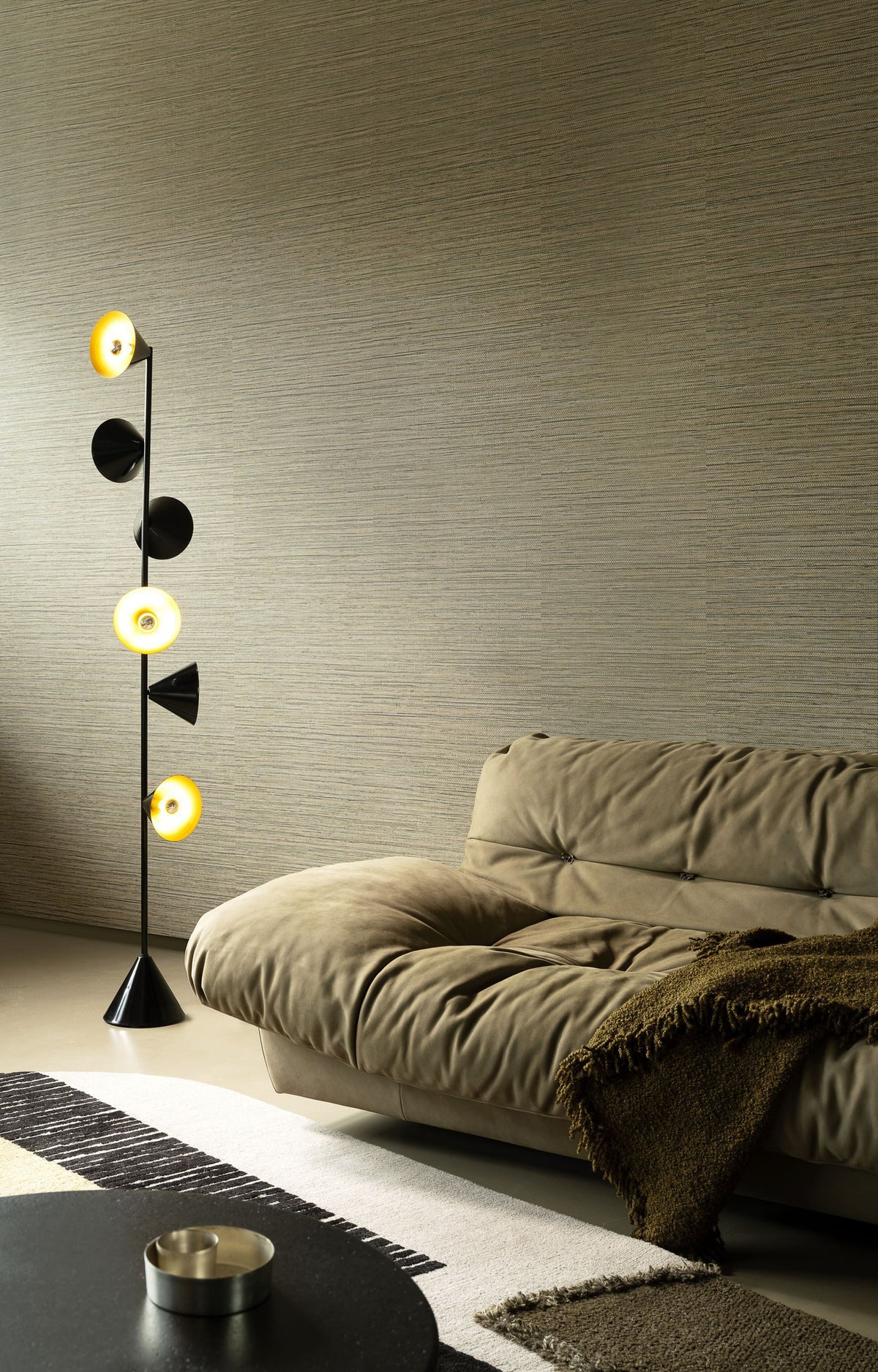 Sombra wallpaper by Arte in Beige – Camouflage behind an olive sofa and a floor lamp