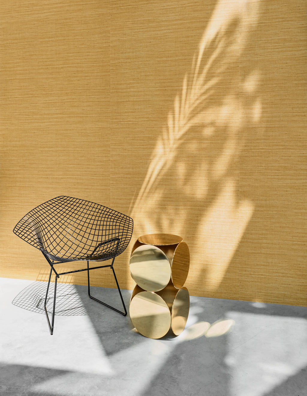Lignes wallpaper by Arte in Gold behind a wire chair and brass side tables