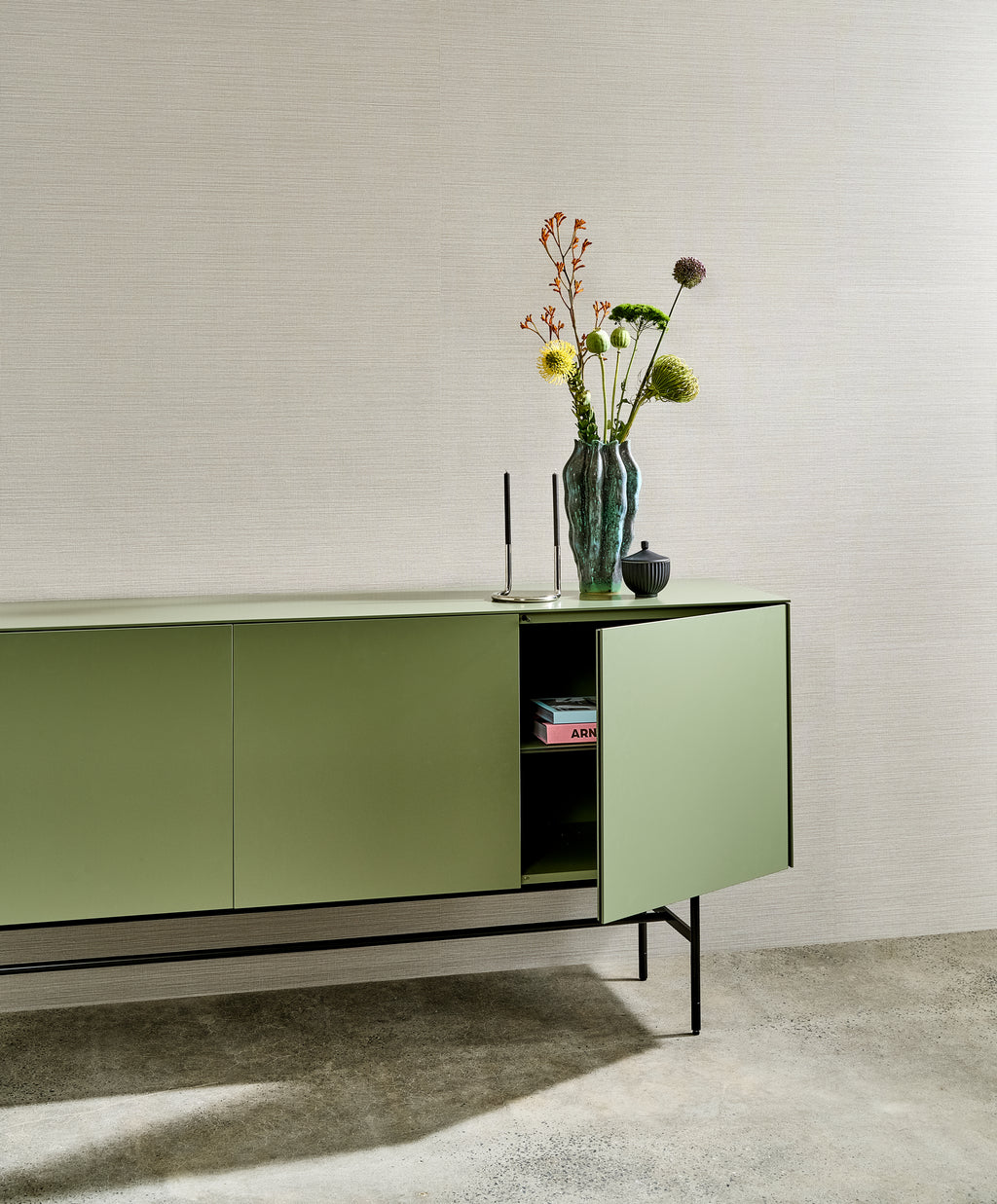 Marsh wallpaper by Arte in Beige – White Smoke behind a green sideboard with flowers