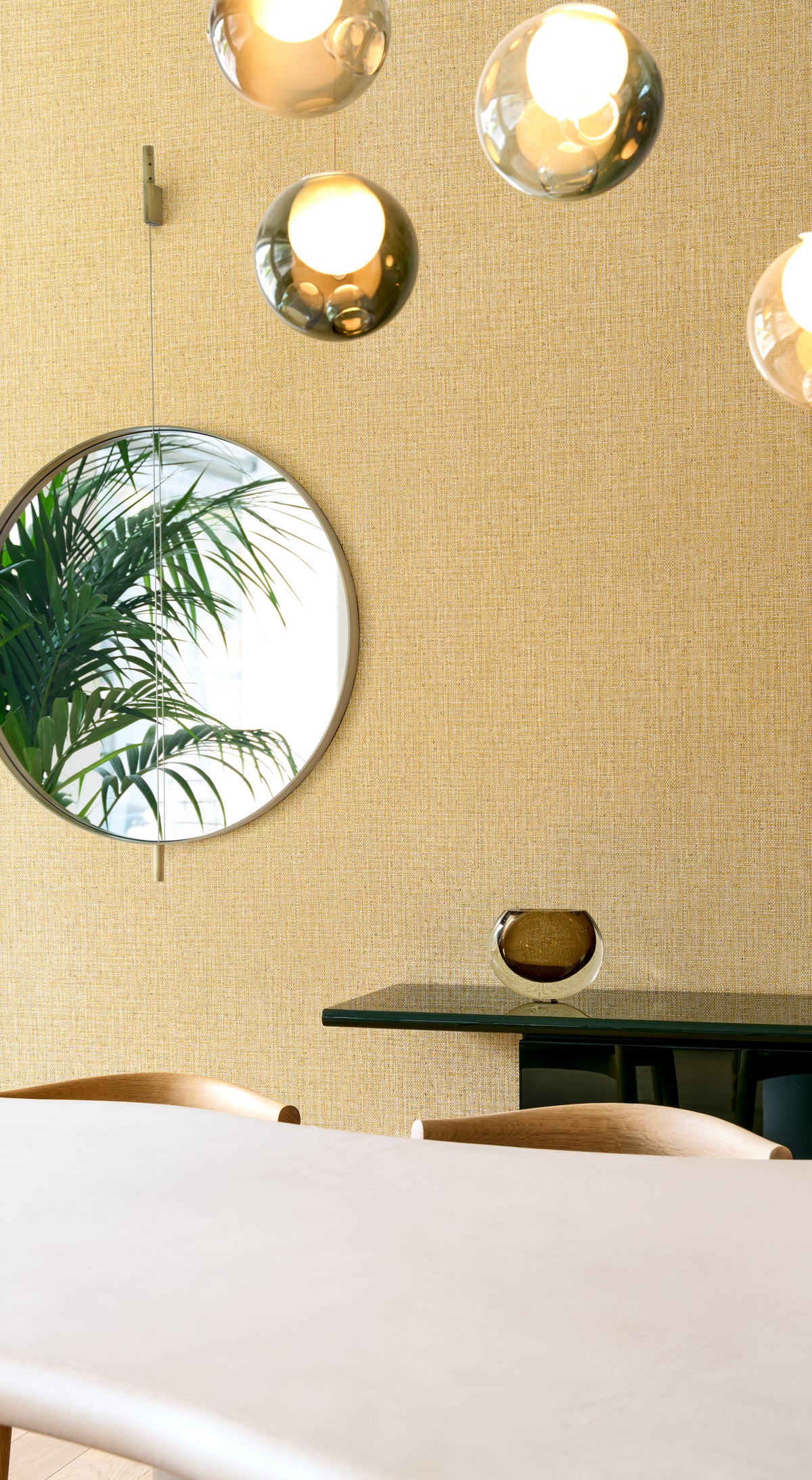 Nongo wallpaper by Arte in Gold in a dining room with a round mirror and a palm