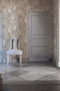 Hiding Hares wallpaper by Emma von Brömssen in beige lining a stone-floored hallway with a white painted chair