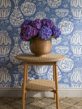 Pottery wallpaper by Långelid/von Brömssen in Blue - abstract design, above a cane stool with a potted hydrangea