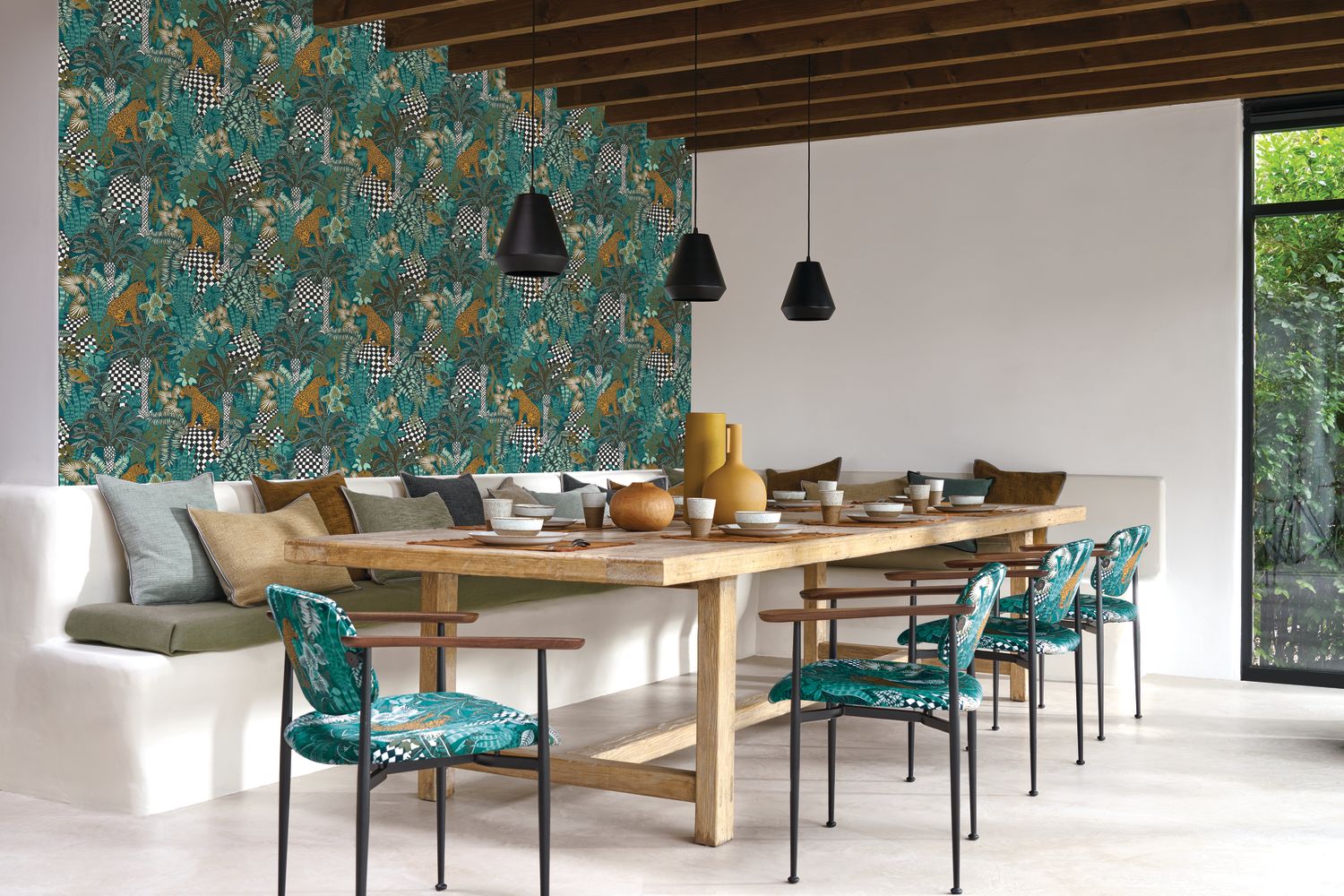 Belize wallpaper by Casamance in teal, a jungle print with leopards and palms styled in a dining room with a long timber table