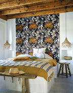 Mirissa wallpaper by Casamance in ink navy and ochre, a palm and blossom print styled behind a bed under timber beams