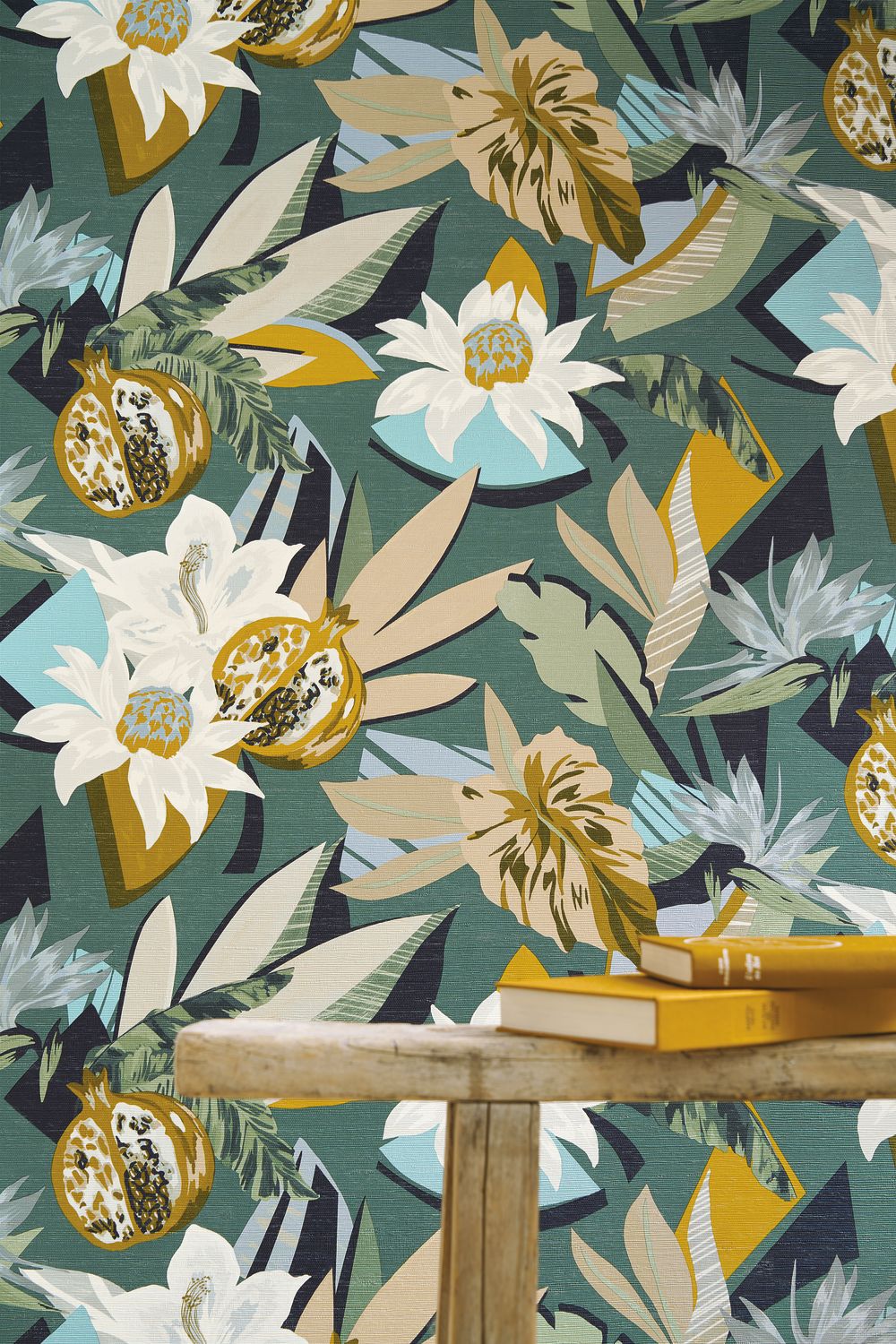 Salvador wallpaper by Casamance in emerald and mustard, a floral and pomegranate print styled behind a bench with books