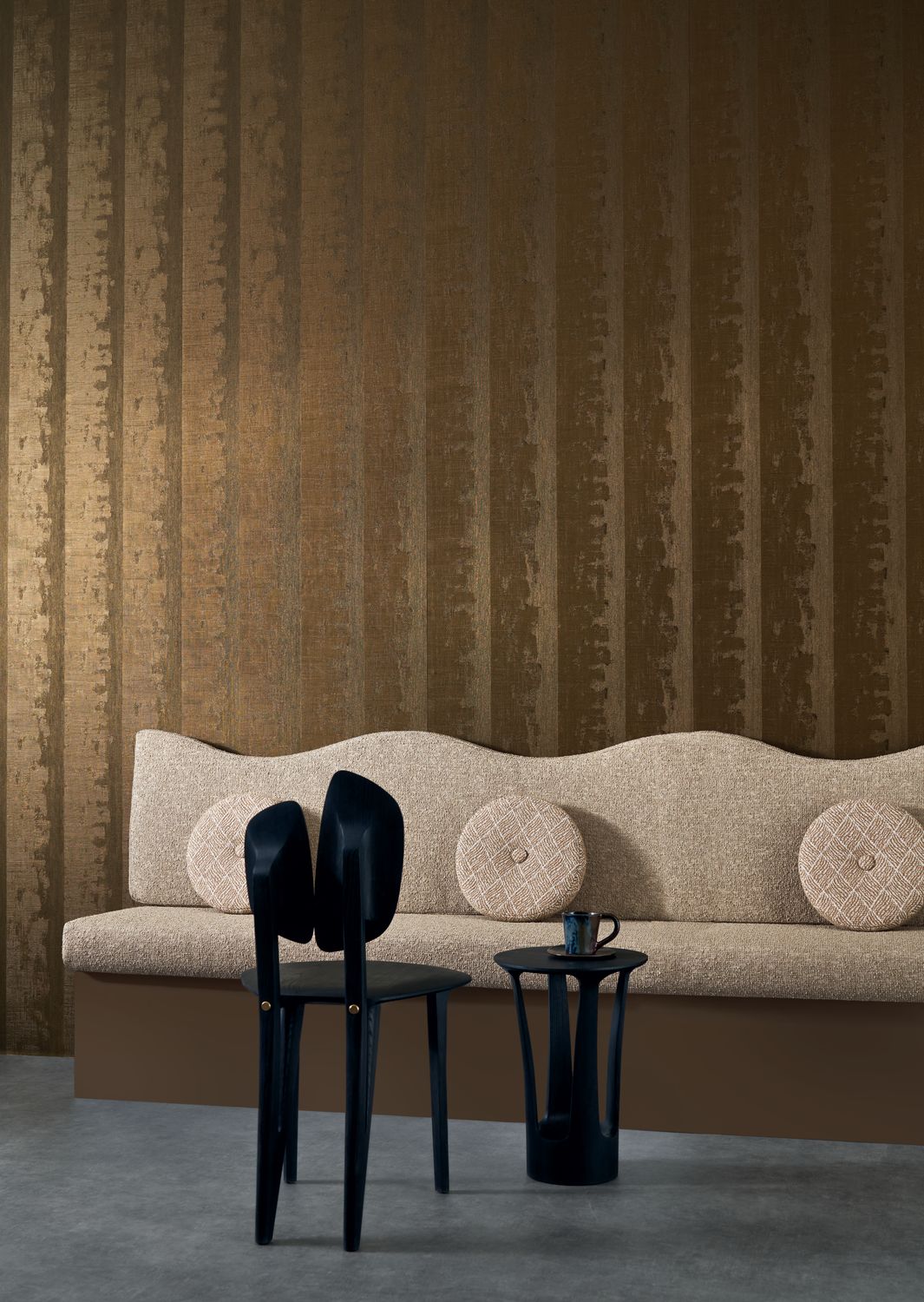 Nerikomi wallpaper by Casamance in dark gold, a vertical striated metallic finish styled behind a curved cream banquette with black sculptural chairs