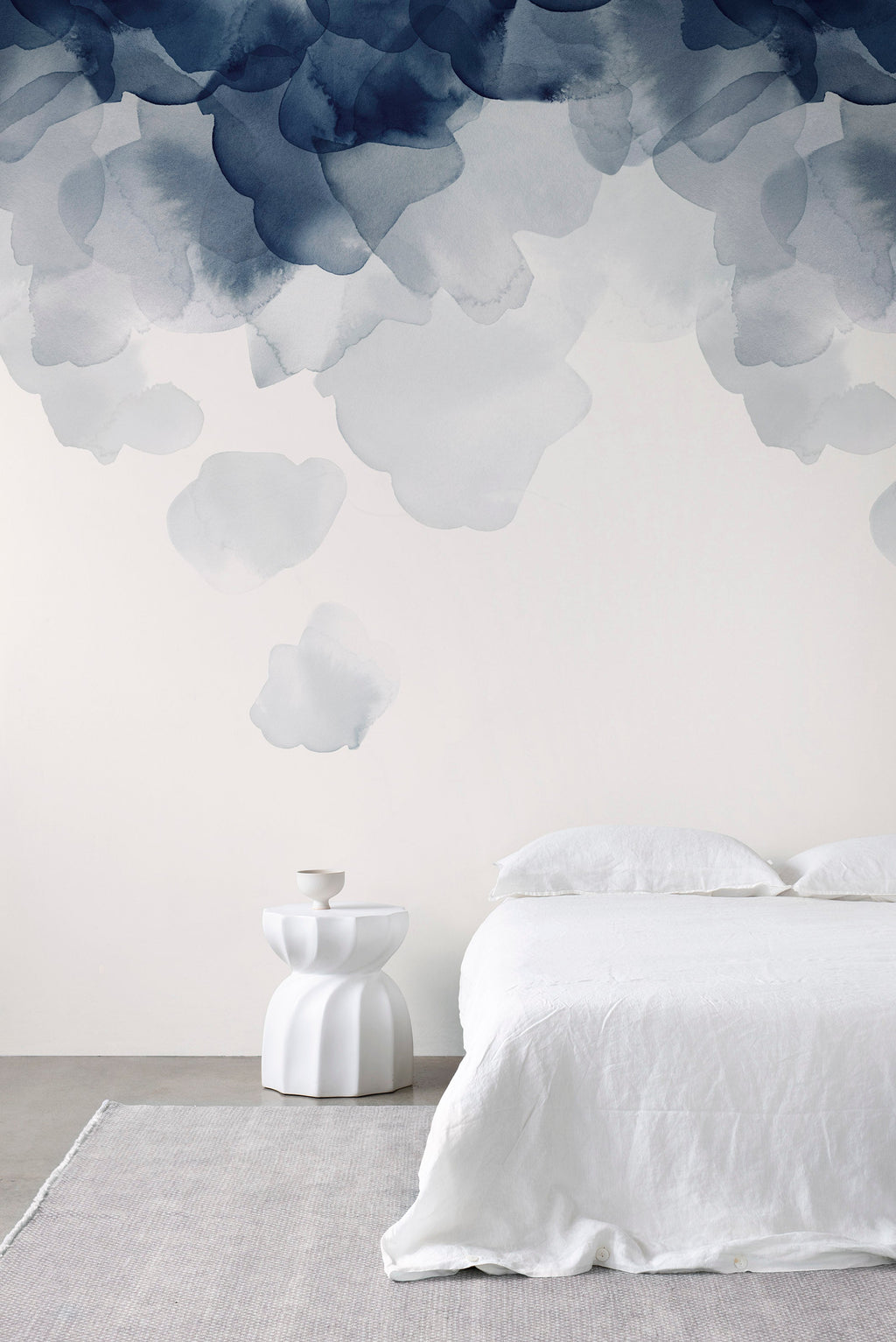 Bloom wallpaper by Emma Hayes in blue, soft watercolour petals cascading down a wall above a white linen bed