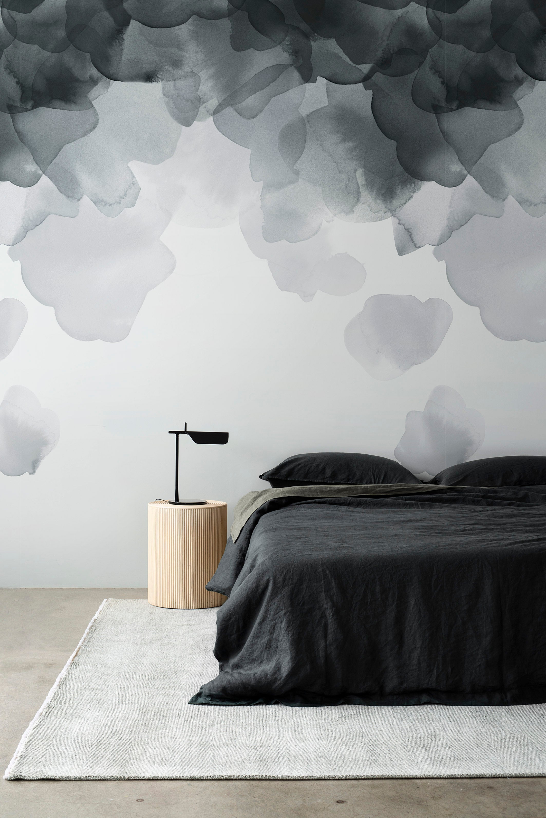 Bloom wallpaper by Emma Hayes in charcoal, watercolour petals above a bed with dark grey linen