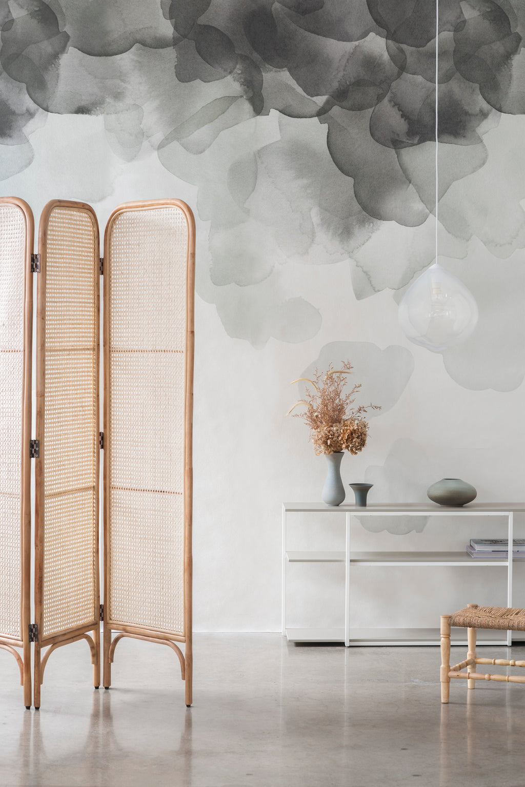 Bloom wallpaper by Emma Hayes in sage, grey-green watercolour petals beside a rattan screen and console