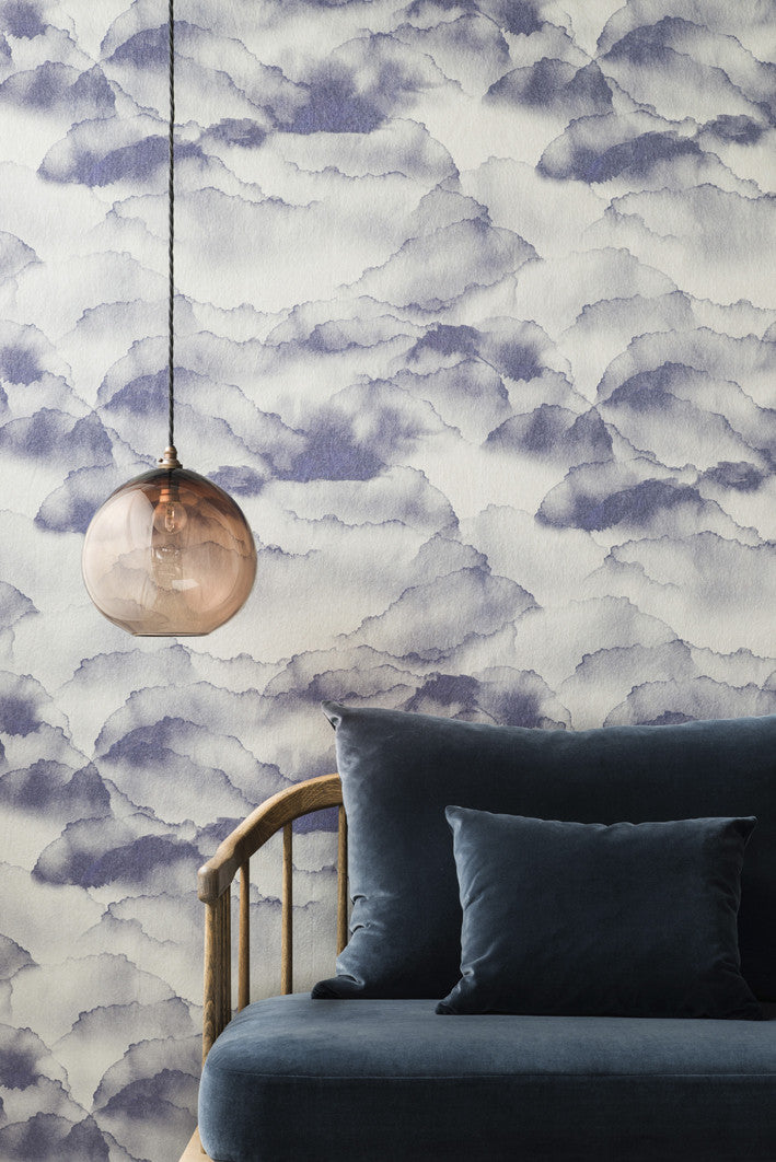 Cloud wallpaper by Emma Hayes in Ash, indigo and blue-grey watercolour clouds styled above a blue velvet sofa with a glass pendant light