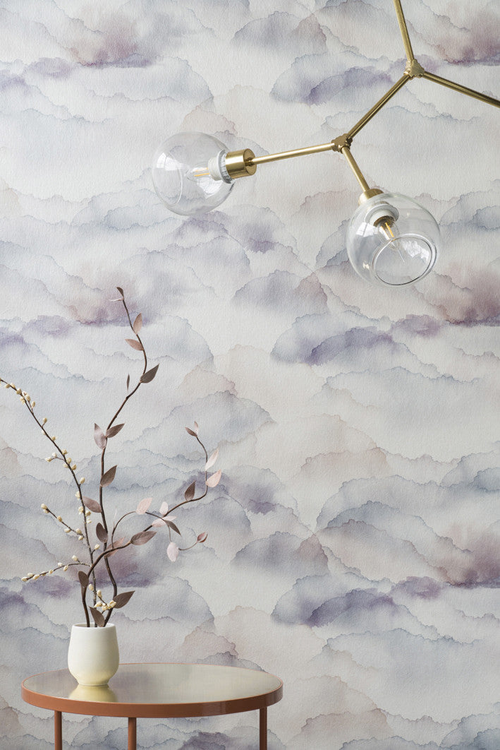 Cloud wallpaper by Emma Hayes in Mauve, soft mauve and grey watercolour clouds behind a brass light and a vase of branches