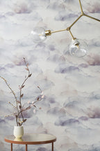 Cloud wallpaper by Emma Hayes in Mauve, soft mauve and grey watercolour clouds behind a brass light and a vase of branches