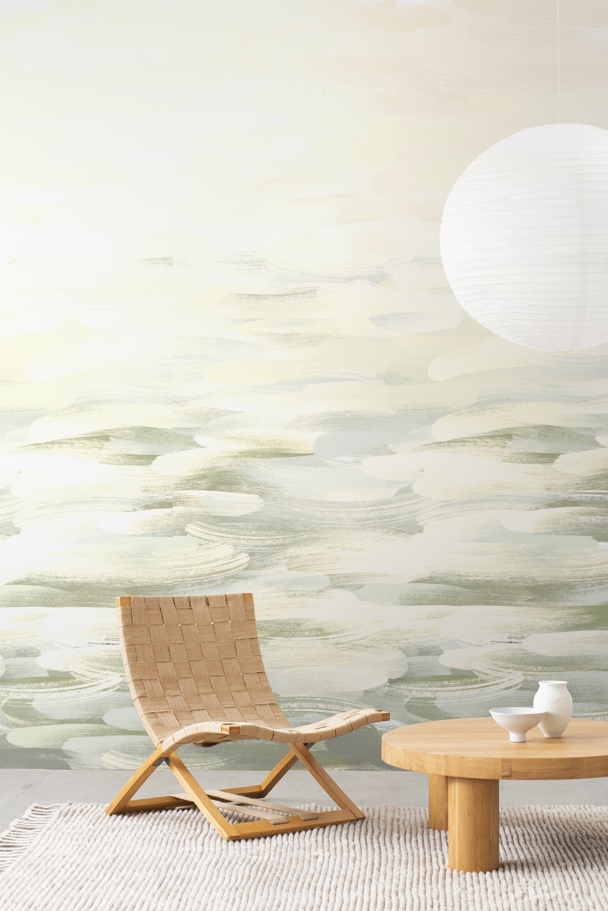 Desertscape wallpaper by Emma Hayes in green, sage and cream brushstroke waves styled in a living room with woven chair and paper lantern