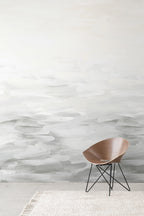 Desertscape wallpaper by Emma Hayes in soft grey and ivory painterly waves behind a wooden bentwood chair on a textured rug