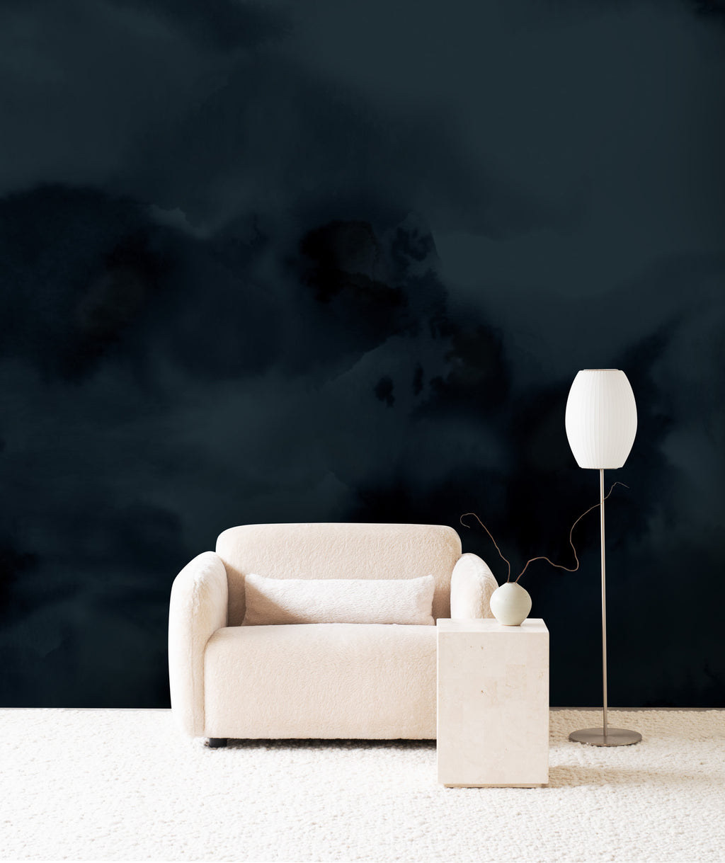 Dispersion wall mural by Emma Hayes in Midnight, deep navy ink clouds behind a cream armchair and floor lamp